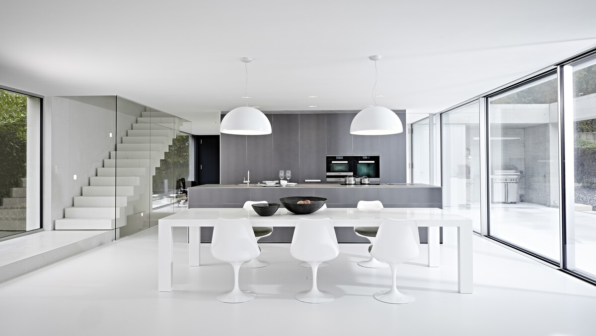 Einen wunderschönen Ausblick genießt man von der Küche aus über das offene Wohn-/Esszimmer nach draußen. Das dunkelgraue Sofa aus der Minotti Collection bietet eine Rückzugsgelegenheit.